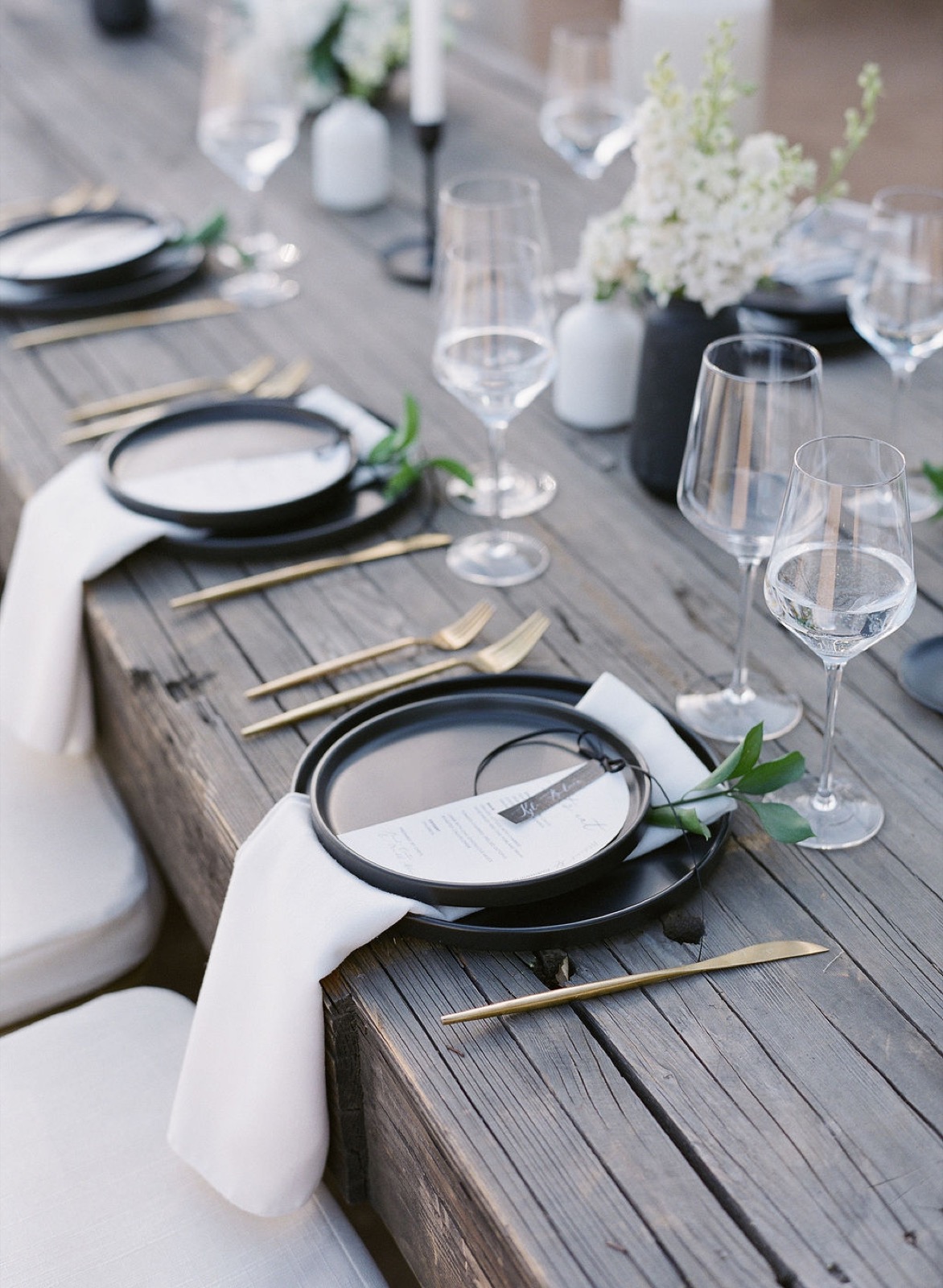 Wedding tablescape with matte black chargers and gold flatware on raw wood